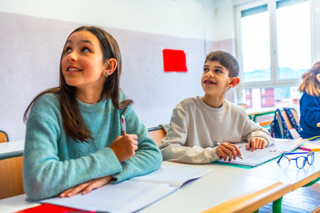 Two young pupils listening to their teacher in elementary school classroom during lesson, education conceptの写真素材