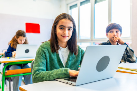 Elementary school student using laptop during class, smiling and looking at camera, with classmates in backgroundの写真素材