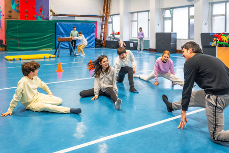Group of smiling students practicing stretching exercises with their teacher during physical...