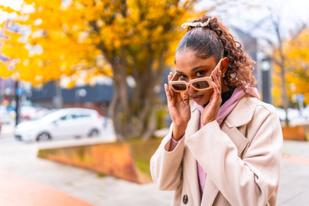 Young african woman with sunglasses and coat in the city in a cold day of autumnの写真素材