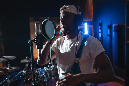 Young black artist wearing headphones and singing into microphone, recording a new album in professional music studioの写真素材