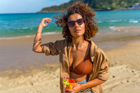 Sensual woman walking along topical beach with a glass of fruitの写真素材