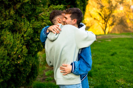 Two men hugging each other tightly in a park, enjoying a tender moment of love and connectionの写真素材