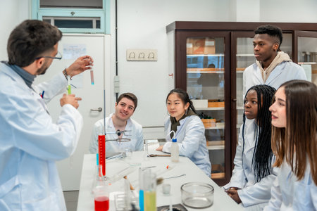 Multi ethnic group of university students attending a chemistry lesson in a laboratory, teacher showing a test tube with a chemical reactionの写真素材