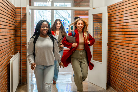 Happy multiethnic students running through a university hallway, celebrating friendship and academic success after an engaging classの写真素材