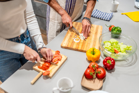 Couple slicing fresh vegetables on wooden cutting boards, preparing a healthy meal together in a modern kitchenの写真素材