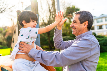 Grandfather and grandson are enjoying time together at the playground, giving a high five and smilingの写真素材