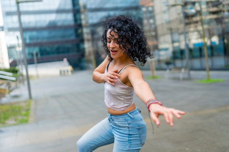 Curly haired woman dancing to lively latin music in an urban city center, soaking up the sun and...