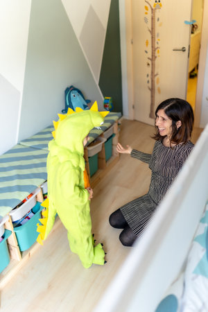 Mother playing with her son wearing a dinosaur costume in his bedroom, having fun togetherの写真素材