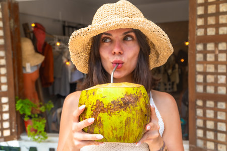 Young woman wearing straw hat enjoying refreshing coconut water during tropical vacation in Siargao island, Philippinesの写真素材