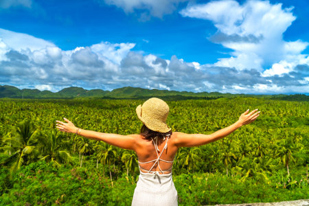 Tourist embracing the stunning view of a vast coconut plantation in Siargao island, Philippines, enjoying the tropical landscape during a sunny dayの写真素材