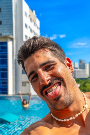 Young man wearing shell necklace sticking out his tongue by hotel rooftop pool in Cebu City, Philippinesの写真素材
