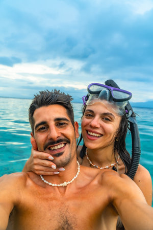 Happy couple taking a selfie while snorkeling in tropical turquoise water, enjoying their vacation in a beautiful seascapeの写真素材