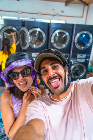 Happy couple wearing motorcycle helmets taking a selfie sticking out their tongues in a laundromatの写真素材
