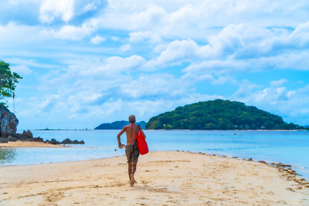 Lifeguard running on a pristine beach towards the sea, carrying snorkeling equipment and a red waterproof bag, in Coron, Philippinesの写真素材