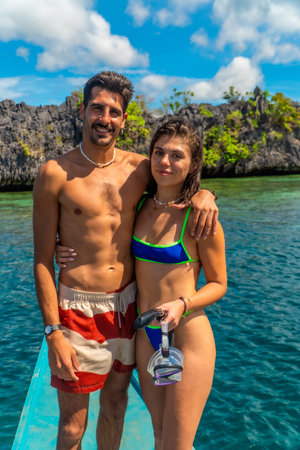 Young couple standing on boat with snorkeling gear, enjoying breathtaking view of turquoise water...