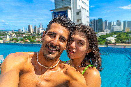 Tourists enjoying holidays in a rooftop swimming pool in Cebu City, Philippines, taking a selfie with cityscape in the backgroundの写真素材