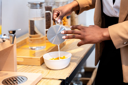 Businesswoman pouring milk into a bowl of cereal, enjoying breakfast during a business tripの写真素材