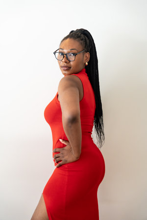 Stylish businesswoman wearing a red dress and glasses, posing confidently during her business tripの写真素材