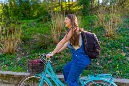 Young woman riding a light blue bicycle through a park, basking in the warmth of a sunny day and enjoying the vibrant outdoorsの写真素材