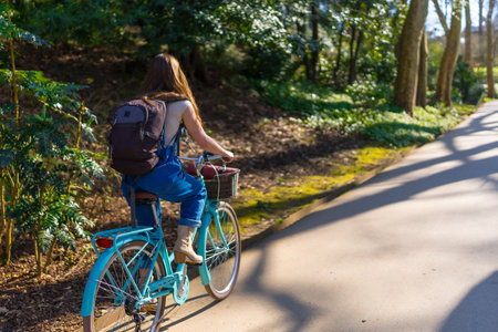 Young woman with backpack riding light blue bicycle in park during sunny day, enjoying freedom and natureの写真素材