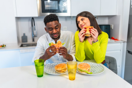 Young multiethnic couple savoring delicious burgers together in their contemporary kitchen, enjoying a relaxed and happy mealtimeの写真素材