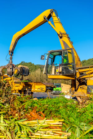Vertical full length photo of a manual male worker driving an excavator working outside a recycling...