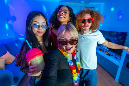 Group of cheerful multi ethnic friends taking a selfie at a vibrant home party, enjoying drinks and colorful disco lightsの写真素材
