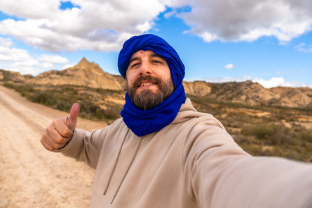 Tourist wearing blue turban showing thumbs up while taking a selfie in Bardenas Reales desert,...