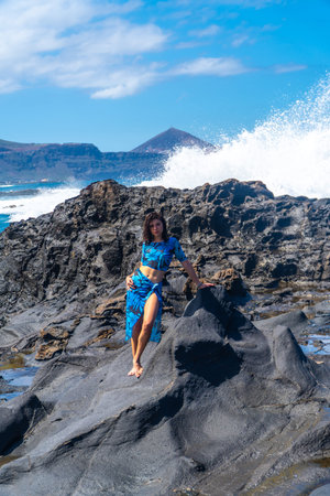 Fashion model posing on volcanic rocks with big waves crashing in the background during a sunny day...