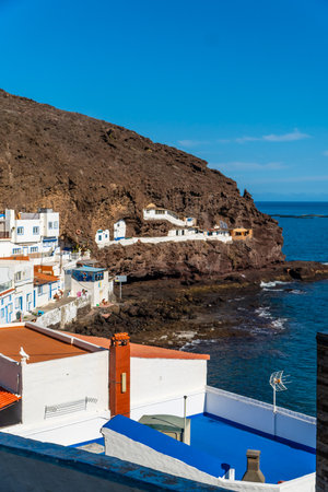 White houses clinging to a rocky coastline under a deep blue sky, creating a picturesque scene of coastal living in Tufia, Gran Canariaの写真素材