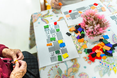 Elderly woman concentrating on bingo game, demonstrating cognitive engagement and social interaction in a nursing home environmentの写真素材
