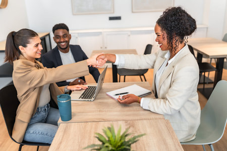 Businesswomen shaking hands after reaching an agreement during a meeting in a modern office,...