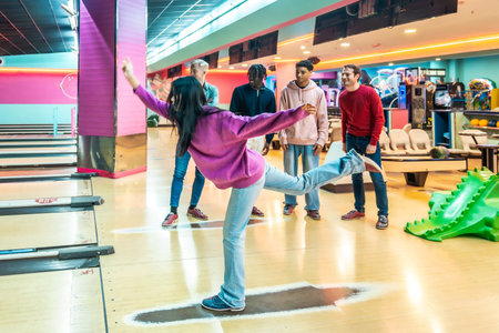 Young woman bowling while friends cheer enthusiastically in a lively bowling alley, creating a fun and supportive atmosphere for everyoneの写真素材