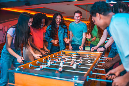 Cheerful multi ethnic friends enjoying a foosball table game in a vibrant entertainment centerの写真素材