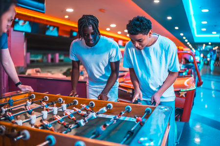 Two young men concentrating on playing foosball in a brightly lit entertainment center, enjoying a friendly competitionの写真素材