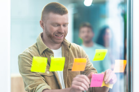 Smiling project manager sticking colorful adhesive notes on a glass wall, brainstorming and planning...