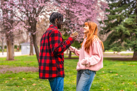 Interracial couple enjoying spring time together in a park, sharing funny content on a smartphone...