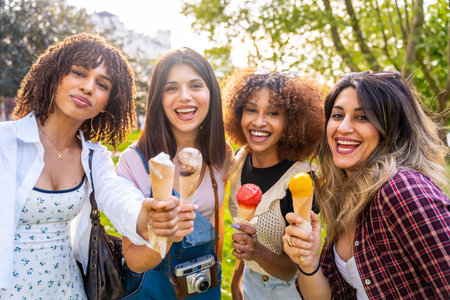 Four cheerful young women enjoying ice cream cones together in a park, celebrating friendship and summer vibesの写真素材