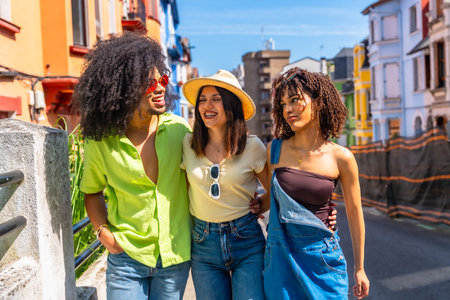 Three happy multi ethnic friends enjoying a sunny day walking and laughing together on a city streetの写真素材