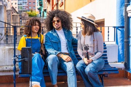 Three young content creators are recording a podcast outdoors, using a smartphone and microphoneの写真素材