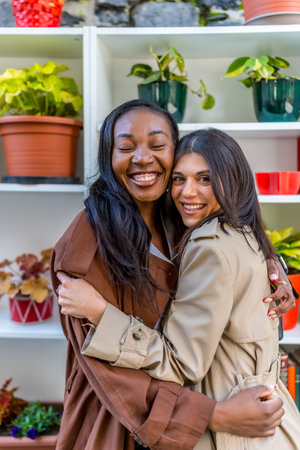 Two multi ethnic female friends are hugging each other with eyes closed in a plant shop, celebrating their friendship and enjoying a relaxing moment togetherの写真素材