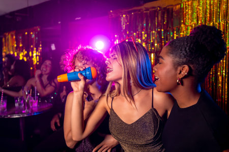 Young women enjoying karaoke night, singing with microphone and having fun with friends in a nightclubの写真素材