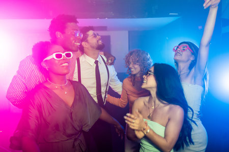Happy multi ethnic friends dancing joyfully together at a vibrant disco party, surrounded by colorful lights and an energetic atmosphereの写真素材