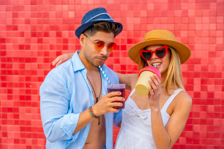 Happy couple enjoying colorful beverages on a summer day, showcasing trendy fashion and a vibrant backdropの写真素材