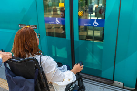 Woman in a wheelchair waits at a train station platform, preparing to board a modern, accessible trainの写真素材