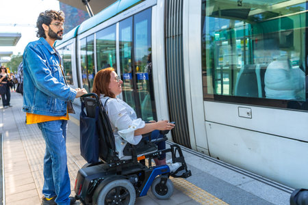 Young man assisting mid adult woman in a wheelchair as they board a modern tram at a bustling city...