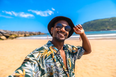 Young man enjoying summer vacation on a sunny beach, happily taking a selfie while surrounded by vibrant tropical sceneryの写真素材