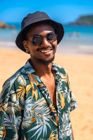 Young man wearing sunglasses and a bucket hat, smiling and enjoying a carefree summer vacation on a beautiful tropical beachの写真素材