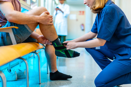 Female nurse bandaging a male patient's injured ankle in a hospital setting, providing support and careの写真素材